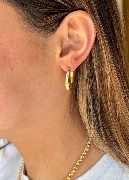 Close-up of an ear wearing a gold hoop earring with a blurred background