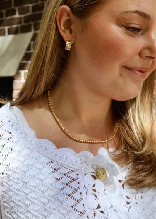 Woman wearing a white lace top with gold jewelry outdoors.