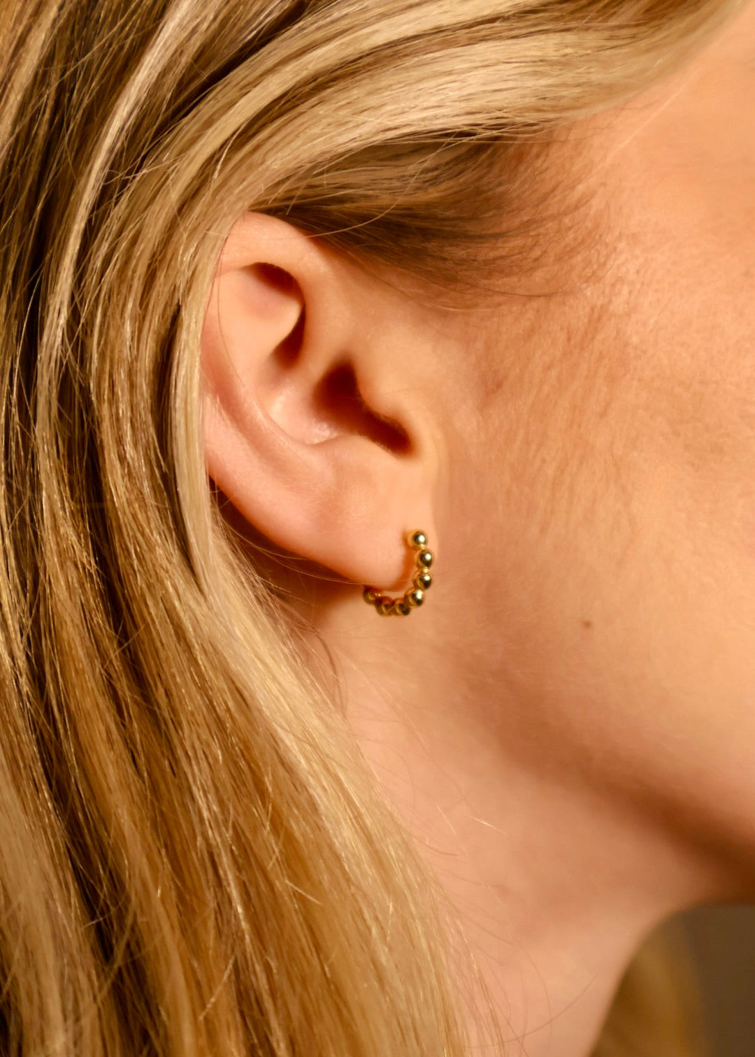 Close-up of a person wearing a gold hoop earring with small beads.