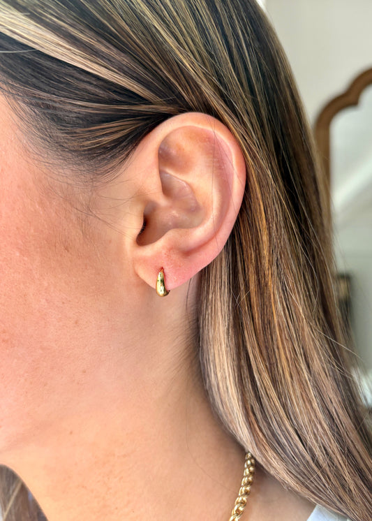 Close-up of a person wearing gold hoop earrings with a neutral background